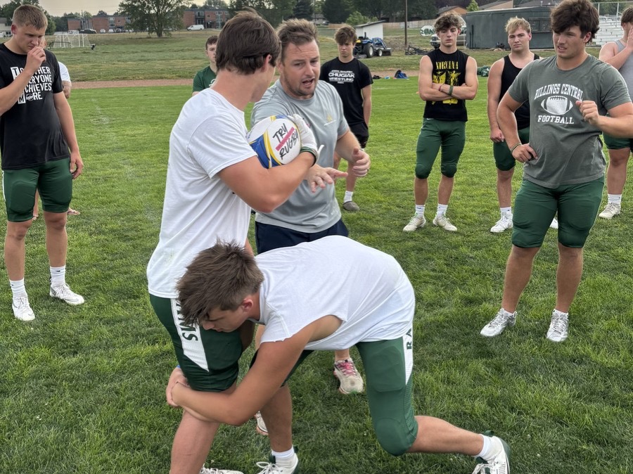Coach demonstrating safe tackle technique to high school football players